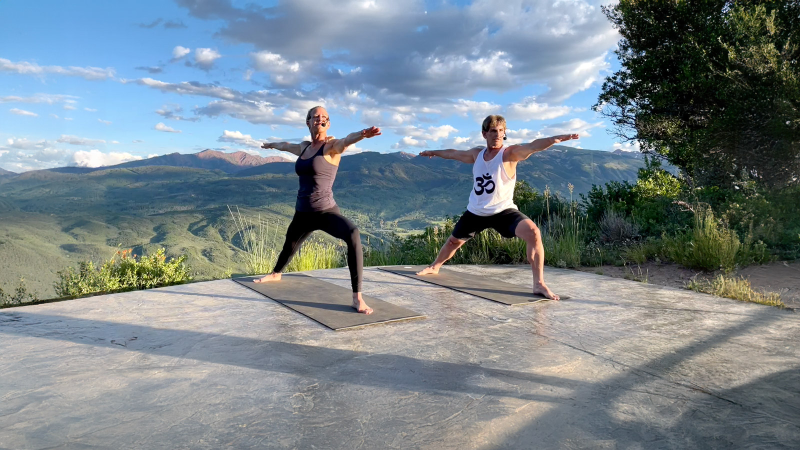 Lori and Jeremy practising yoga on a deck with mountains behind them
